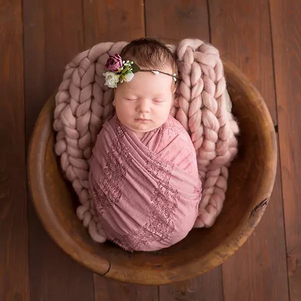 Image of a newborn baby girl at photoshoot swaddled in pink muslin blanket