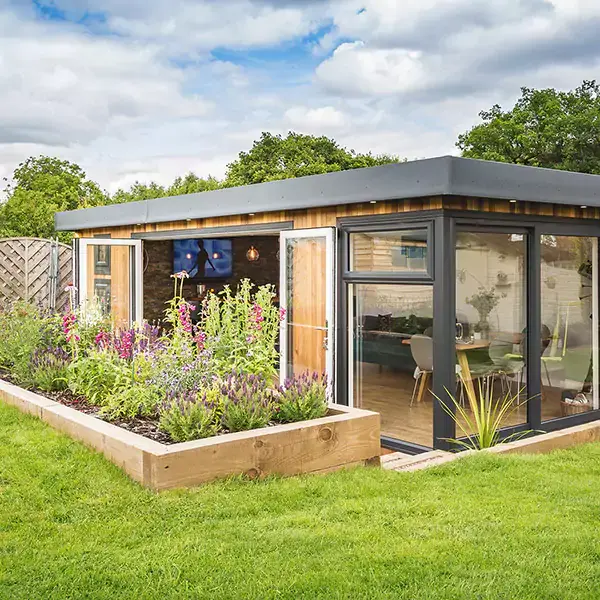 large garden man cave building with open bifold doors and with plant bed and lawn area in front