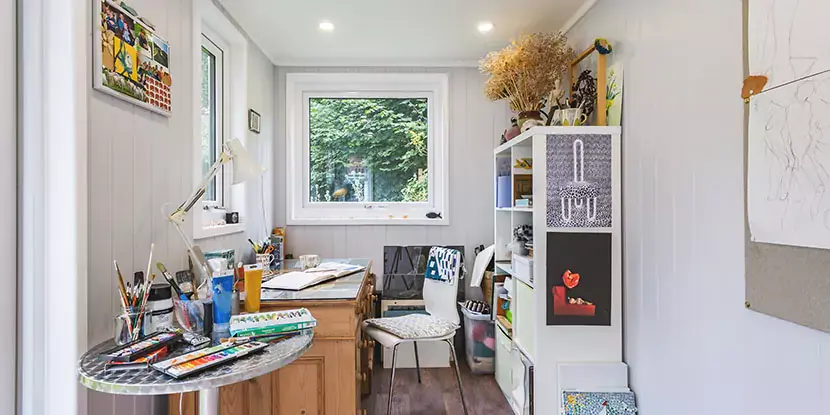 Interior of a garden room artists studio with paints & brushes on desk 