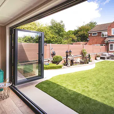 cMarley Cabin Master Building with open Bi-Fold Doors on patio area with rattan table and chairs and foliage in background