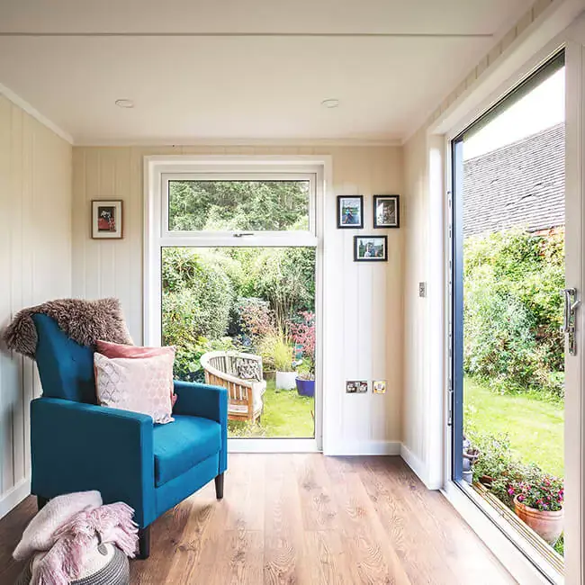 summerhouse garden room with blue armchair and view of lawn 