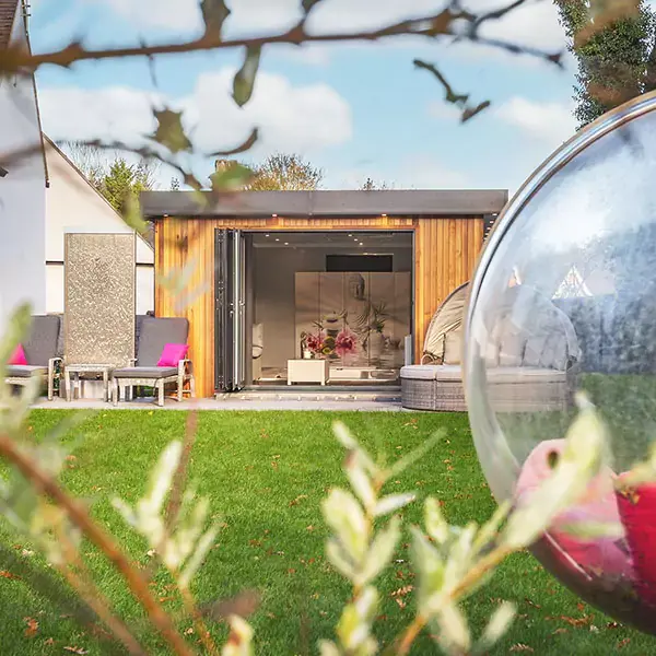 Cedar Garden Building with rattan outside furniture and bright bean bags with patio area and grassy lawn in foreground with view of swim spa and large buddha wall art