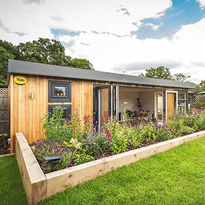 External image of Cabin Master Garden Room with bench in front surrounded by grassy lawn area with potted plant