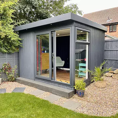 Small Home Office Building Micro Office in garden with potted plants and gravel pathway