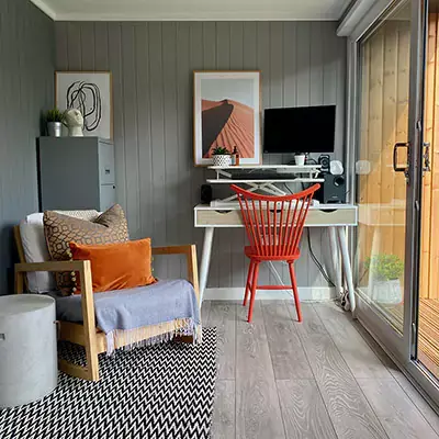 Small Home Office garden building with PC and orange desk chair and corner chair and patterned rug with wall art