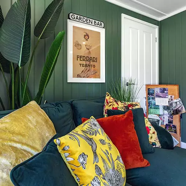 Interior of a garden room with dark green feature wall, tropical plant and plush velvet sofa