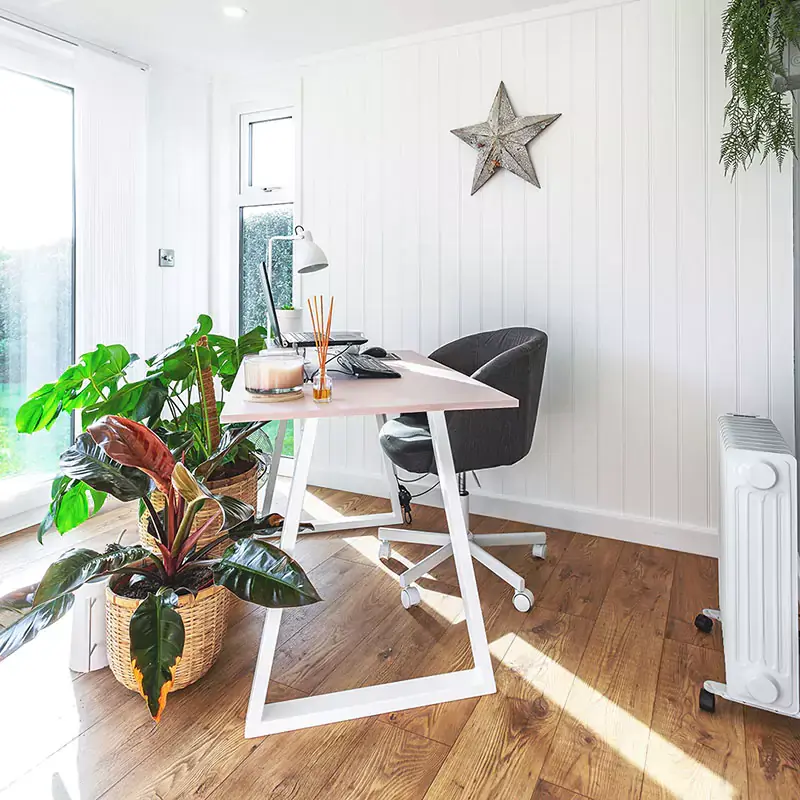 Internal picture of micro office with PC and yellow chairs and wall art and white desk chair and fire place